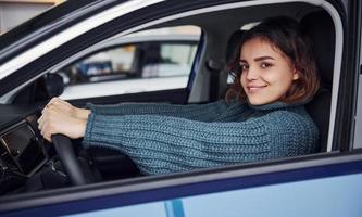 Positive young girl in casual clothes sitting inside of modern car and smiling photo