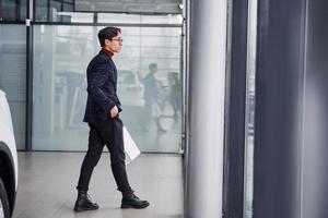 With shopping bags. Young business man in luxury suit and formal clothes is indoors in the office photo