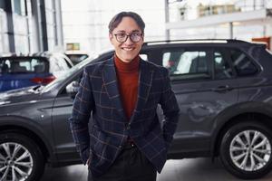 Posing for the camera. Young business man in luxury suit and formal clothes is indoors near the car photo