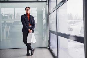 With shopping bags. Young business man in luxury suit and formal clothes is indoors in the office photo