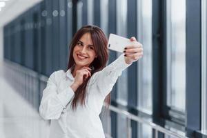 Brunette in white shirt that walks indoors in modern airport or hallway at daytime photo