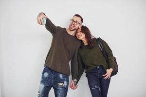 Cheerful multi ethnic couple in casual clothes making selfie indoors in the studio against white background photo