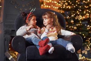 dos niñas sentadas y comiendo galletas en una habitación decorada con navidad foto