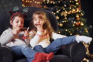 dos niñas sentadas y comiendo galletas en una habitación decorada con navidad foto