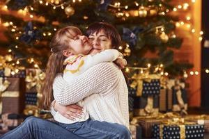 madre abrazando a su pequeña hija en una habitación decorada con navidad foto