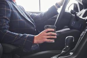 Close up view of men's hand with cup of drink. Guy in formal wear sitting inside of modern new car photo