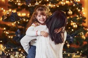 Mother embracing her little daughter in christmas decorated room photo