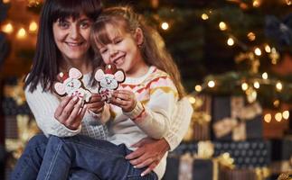 niña con su madre sosteniendo galletas navideñas en las manos foto