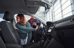 Professional salesman assisting young girl by choosing new modern automobile indoors. Woman sitting inside photo