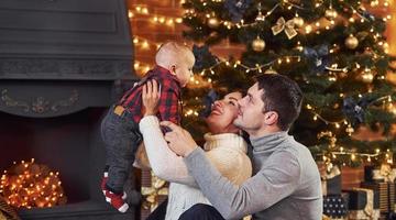 hermosa pareja caucásica celebrando la navidad en el interior con su pequeño hijo foto