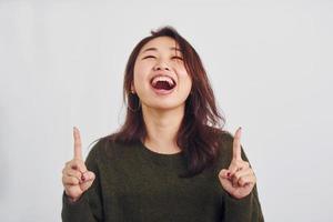 retrato de una joven asiática feliz que apunta al interior del estudio con fondo blanco foto