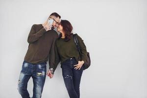 Cheerful multi ethnic couple with backpack and phone standing together indoors in the studio against white background photo