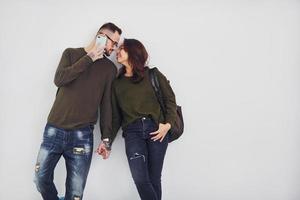 Cheerful multi ethnic couple with backpack and phone standing together indoors in the studio against white background photo