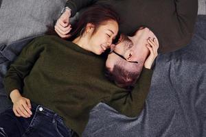 Happy multi ethnic couple in casual clothes lying down together indoors in the studio. Caucasian guy with asian girlfriend photo