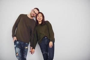 feliz pareja multiétnica con ropa informal está junta en el interior del estudio. chico caucásico con novia asiática foto