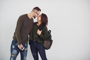 Cheerful multi ethnic couple with backpack and phone standing together indoors in the studio against white background photo