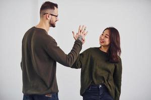 Cheerful multi ethnic couple in casual clothes giving high five indoors in the studio against white background photo