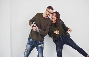 Cheerful multi ethnic couple with backpack and phone standing together indoors in the studio against white background photo