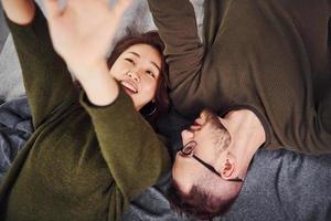 feliz pareja multiétnica con ropa informal acostada juntos en el interior del estudio. chico caucásico con novia asiática foto