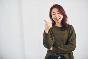 Portrait of happy asian young girl that shows thumb up indoors in the studio against white background photo