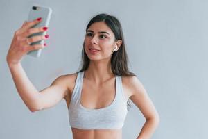 Young beautiful brunette in underwear and in headphones and with phone is indoors in the studio against white background photo