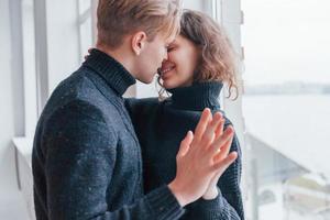 Cute young couple kissing each other indoors near the window photo