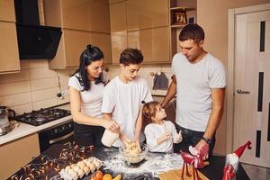 la familia feliz se divierte en la cocina y prepara la comida foto