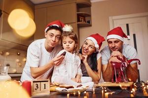 Festive family in christmas hats have fun on the kitchen and preparing food photo