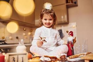 linda niña sentada y diviértete en la cocina con comida foto