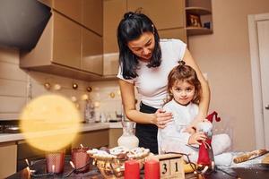 Mother with her little daughter preparing food on kitchen and have fun photo