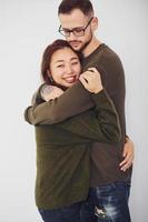Happy multi ethnic couple in casual clothes embracing each other indoors in the studio. Caucasian guy with asian girlfriend photo