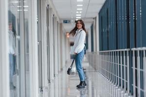 Brunette in white shirt walks indoors in modern airport or hallway at daytime photo