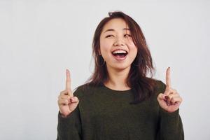 retrato de una joven asiática feliz que apunta al interior del estudio con fondo blanco foto