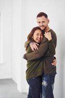Happy multi ethnic couple in casual clothes embracing each other indoors in the studio. Caucasian guy with asian girlfriend photo