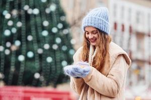 Young positive girl holds little gift box in hands outdoors in the city photo