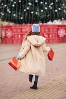 Rear view of young girl in warm clothes and with shopping bags in hands that have a walk outdoors in the city photo