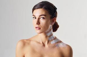 Naked woman with paint on neck is in the studio against white background photo