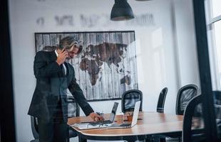 Mature businessman with grey hair and beard in formal clothes have conversation by the phone in the office photo