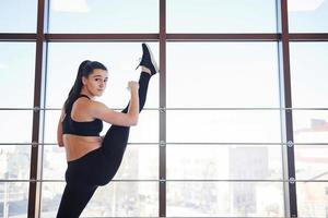 Brunette leaning on the railings of window and doing long stretching for legs photo