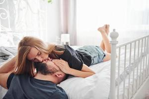 joven pareja casada besándose en el dormitorio durante el día foto