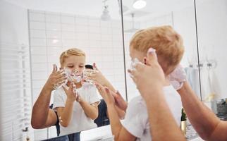 Father with his son is in the bathroom have fun by using shaving gel and looking in the mirror photo