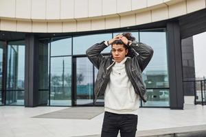 Handsome young man with curly black hair standing and feels shoked on the street against building photo