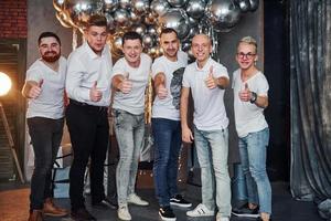 grupo de hombres alegres parados juntos en una habitación decorada con navidad y posando para una cámara foto