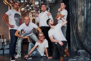 grupo de hombres alegres parados juntos en una habitación decorada con navidad y posando para una cámara foto