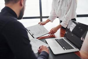 Woman and man in formal clothes working together indoors in the office by table with documents photo