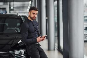Young man in formal clothes is near brand new expensive car photo