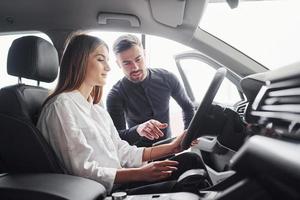 Woman testing car by help of male assistant indoors in the salon photo