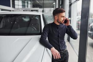 un joven con ropa formal está cerca de un coche nuevo y caro foto