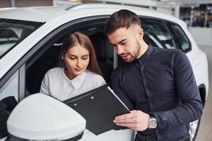 Woman testing car by help of male assistant that shows doments indoors in the salon photo