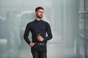 Young bearded guy in elegant clothes standing indoors against grey background photo